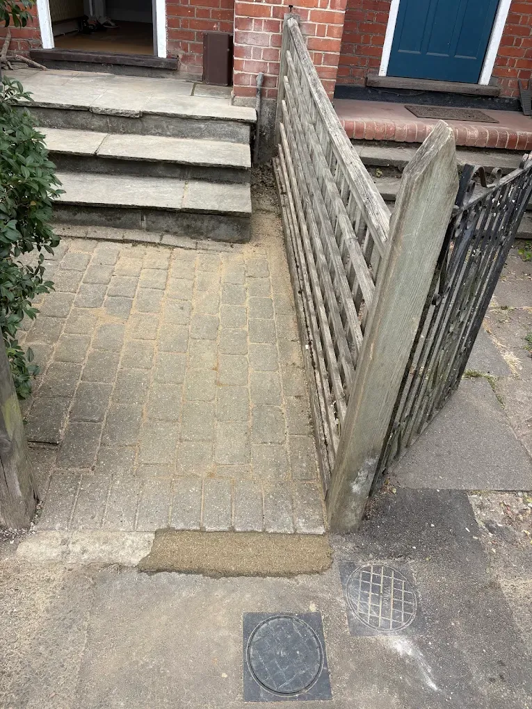 A front path beside a fence after the work, with a new stop tap cover set in at the gate