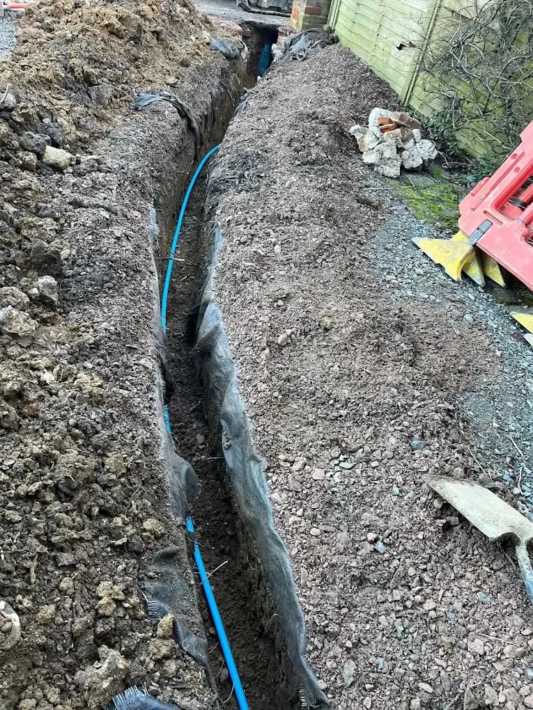 New blue water pipe snaking along a trench through a gravel path, lined with membrane