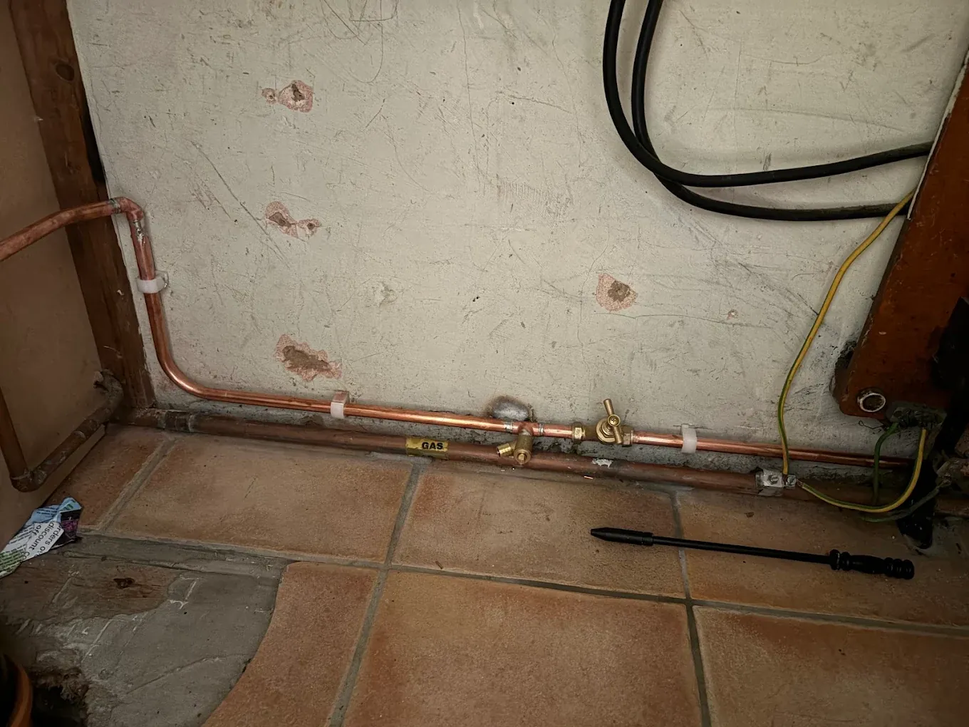 Copper pipework running along the foot of a wall inside a utility room, with a stop tap and an incoming supply