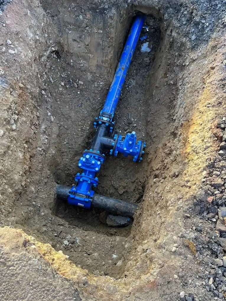 A blue valve fitted on a black water main in the bottom of a deep trench