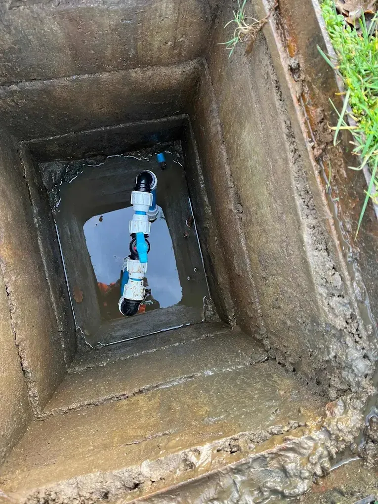 Looking down into a concrete meter chamber at new white fittings on a blue supply pipe