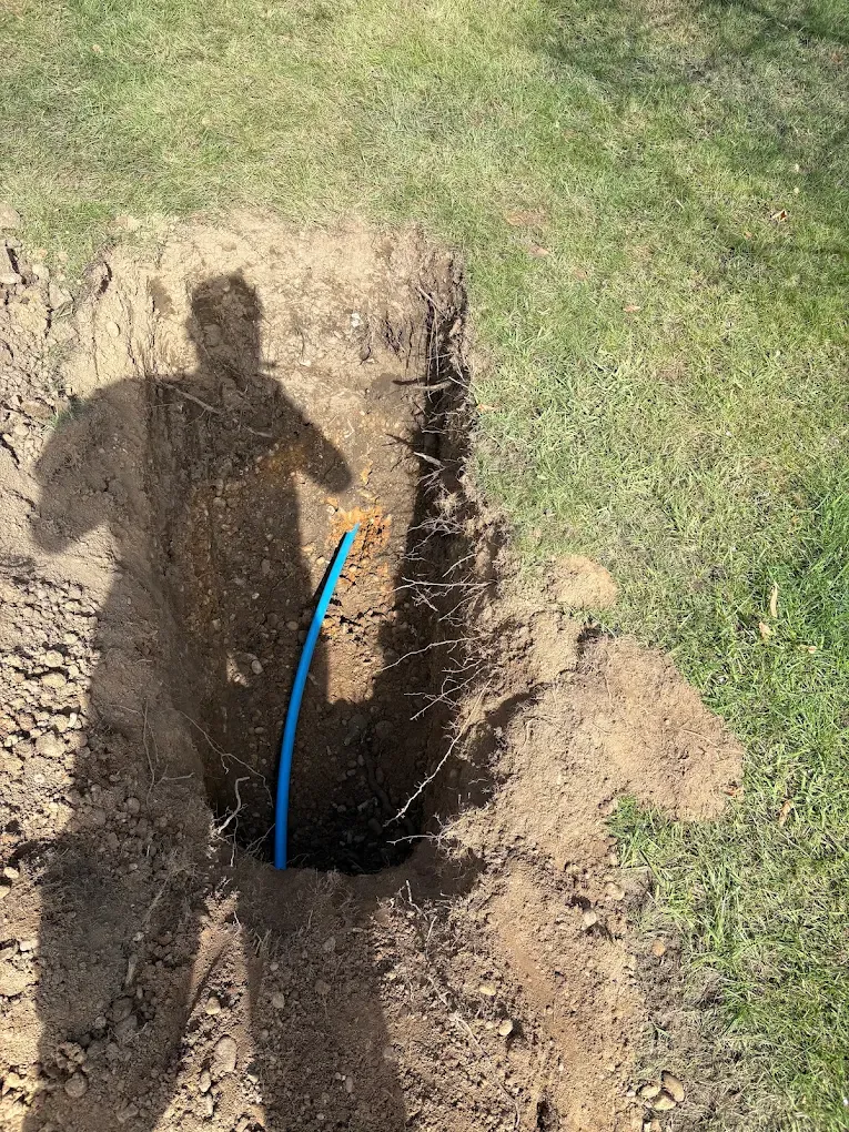 A narrow pit dug at the edge of a lawn with new blue pipe rising out of the bore at the bottom