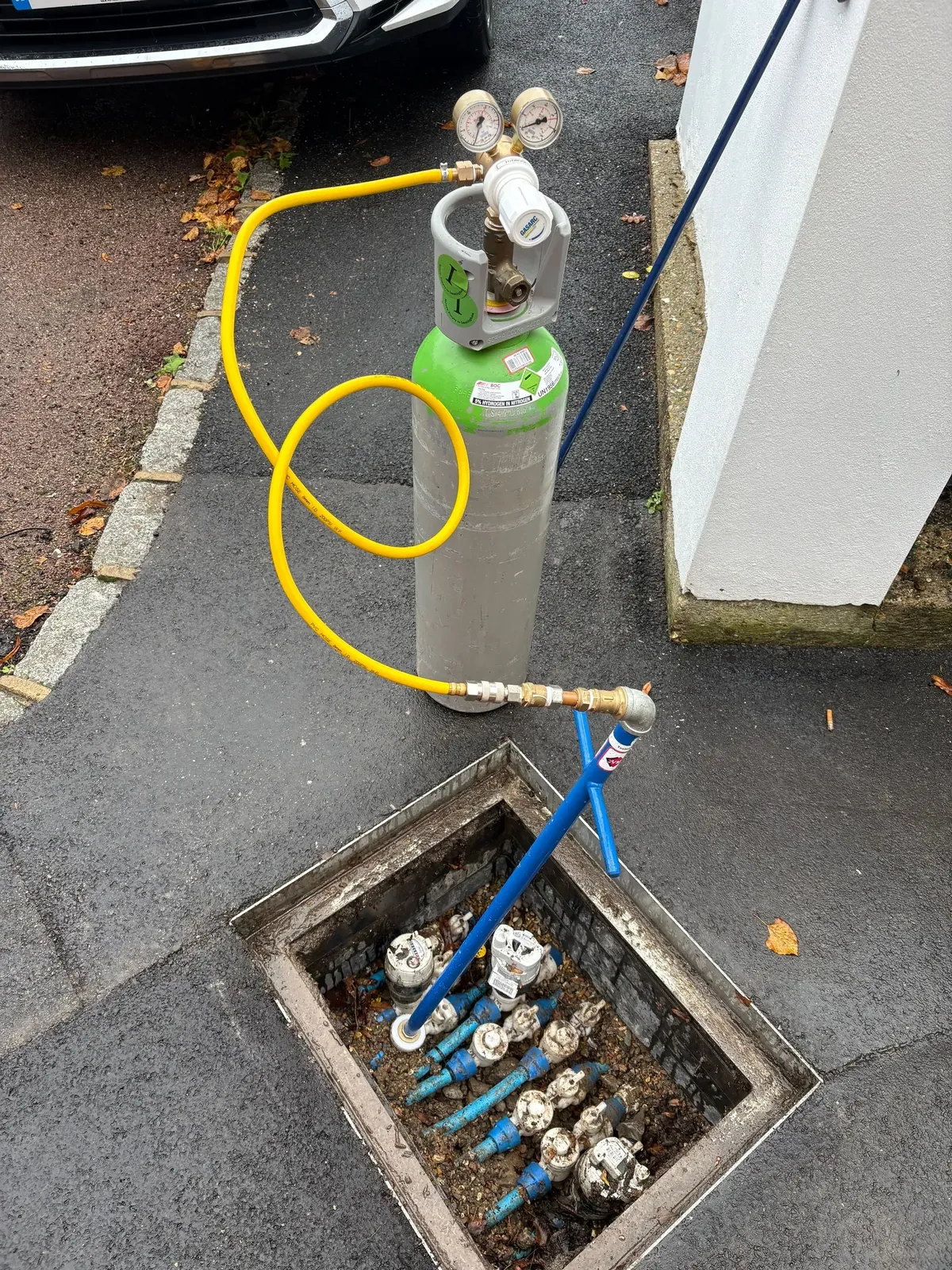 A tracer gas cylinder with a yellow hose running into a pavement chamber holding a row of blue water meters